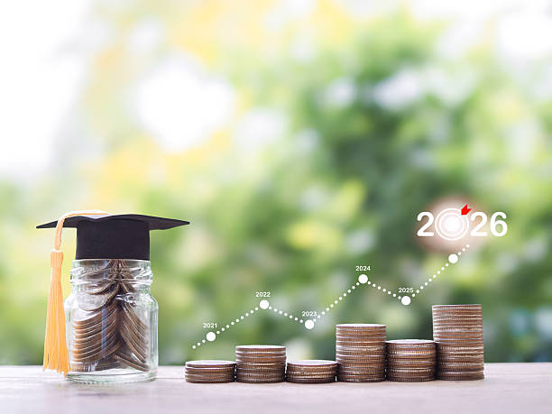 istock Glass bottle with graduation hat and stack of coins with virtual increasing graph. The concept of saving money for education, student loan, scholarship, tuition fees in year 2026. 2232863770