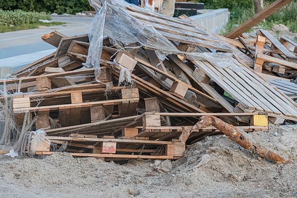 istock Stack of worn wooden crates, partially covered with torn plastic sheeting, against a backdrop of greenery and an unfinished structure Natural daylight from the upper left corner creates uneven illum 2232864493