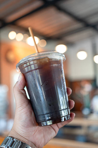 Hand holding a plastic cup filled with iced americano coffee.