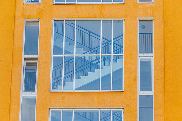 Modern urban building facade with central, blue-stepped staircase and yellow back wall, viewed from street level, daytime lighting.