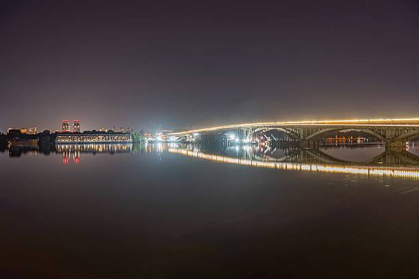 istock Calm river at night, with a lit bridge spanning it The bridge reflects light onto the water, creating symmetry Buildings or more bridges are visible in the distance Dominant color palette is muted 2232867035