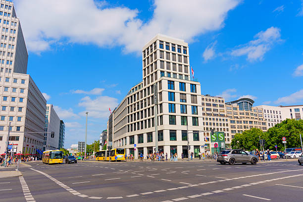 Berlin, Germany - August 16, 2025: Vibrant urban scene featuring modern architecture at Leipziger Platz, bustling traffic, and pedestrians against a backdrop of bright blue skies and white clouds.