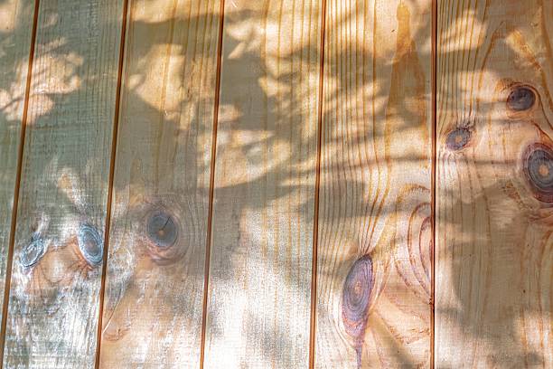 Close-up view of a stained wooden deck under dappled sunlight, with tree branches overhead a