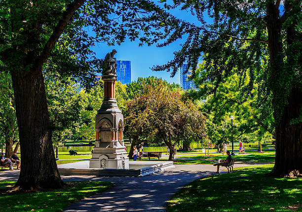 Boston, Massachusetts, USA - August 26, 2025: The Ether Monument, located towards the corner of Arlington and Beacon streets in the northwest corner of the garden, commemorates the first use of ether as an anesthetic. Designed by John Quincy Adams Ward and gifted to the city on June 27, 1868, by Thomas Lee, it is the oldest monument in the garden. Standing 30 feet tall and made of granite and red marble, the statue's carved figures tell the Parable of the Good Samaritan. Established in 1837, the Public Garden is a large park in the heart of Boston, adjacent to Boston Common. It is a part of the Emerald Necklace system of parks. The Public Garden was the first public botanical garden in America.