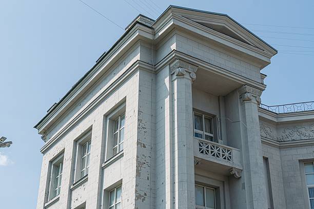 istock Light-colored, classical urban building with columns, pediment, ornamentation, multiple windows, stone frames, under clear midday sky 2232868399