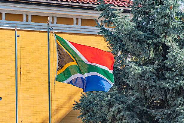 istock Outdoor scene during daylight, three South African flags against a light brick wall with dark horizontal band Vivid colors orange, white, green, black, blue Angled view from below, partially visib 2232870021