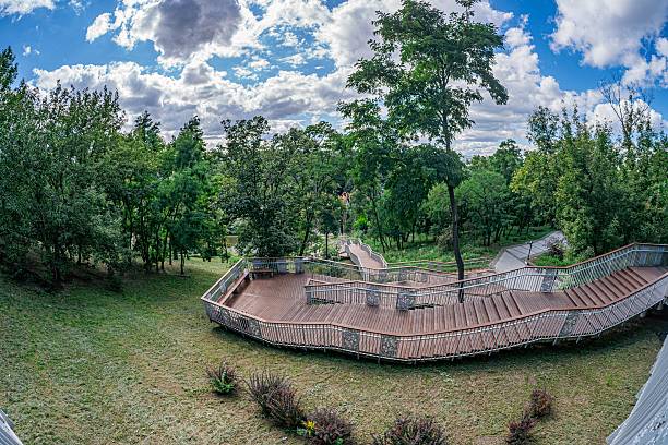 istock A modern city park scene during twilight, featuring a multi-level wooden pavilion and winding path amidst green trees Soft, diffused lighting with a blue-to-yellow gradient sky 2232870136