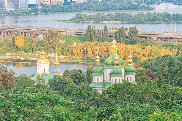 istock Tranquil Kyiv panorama featuring a large green-white domed church on a hillside, flanked by lush vegetation and another smaller structure with similar architecture Calm waterbody partially obscured 2232875975