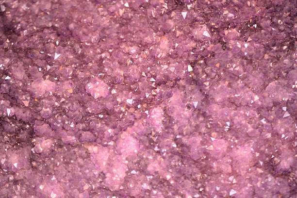 A vibrant, full-frame macro shot of a geode filled with sparkling amethyst crystals. The crystals vary in size and clarity, creating a mesmerizing texture of purples and pinks, catching the light with a glittery effect.