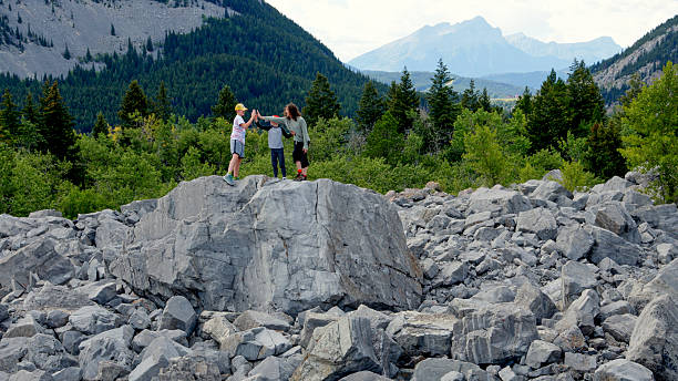 Brothers on top of boulder, mountains and forest in distance, Frank Slide boulder field, Crowsnest Pass, Canadian Rockies, Alberta