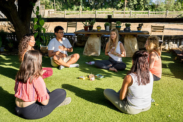 istock Group of adults sitting in a circle on a lawn practicing mindfulness during a systemic therapy session with horses, in the background a paddock fence and a table 2232883395