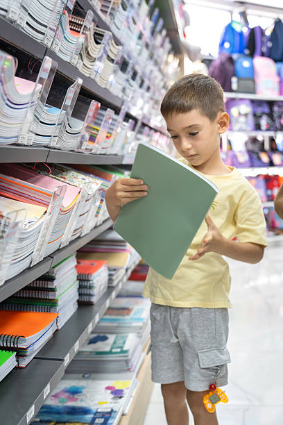 istock Elementary School Child standing in bookstore and looking for notebooks and books. Back To School Shopping Concept. Shopping for school. Little boy trying to decide which notebook to buy. 2232889935