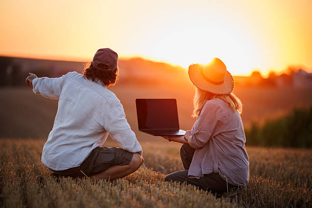 istock Two farm workers using laptop for smart farming analysis while looking at farmland during sunset 2232889996