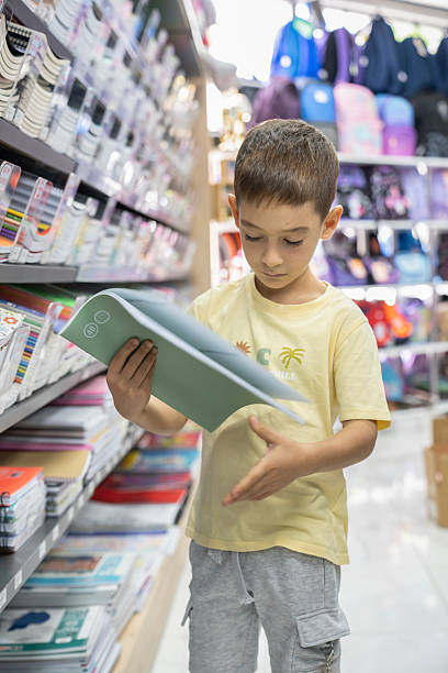 istock Elementary School Child standing in bookstore and looking for notebooks and books. Back To School Shopping Concept. Shopping for school. Little boy trying to decide which notebook to buy. 2232890101