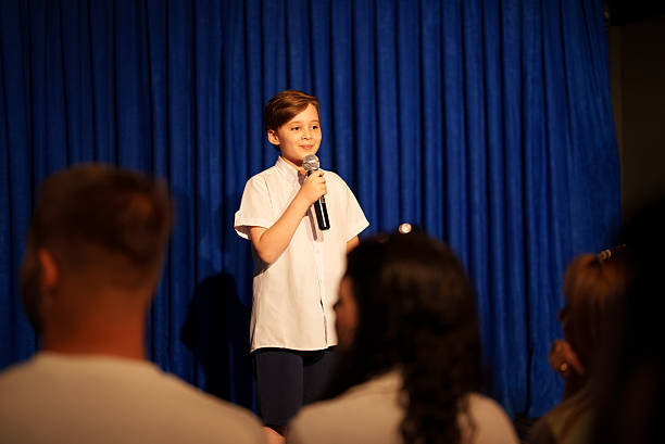 istock Boy speaking on stage with microphone in front of audience 2232894626