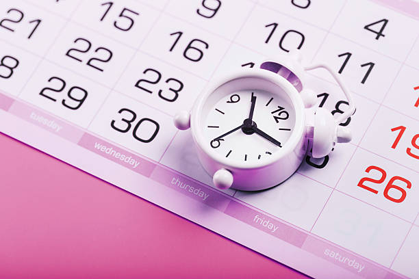istock White alarm clock and calendar on a pink desktop background. 2232899576