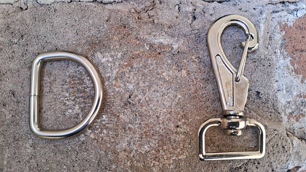 Close-up of a metal D-ring and swivel hook placed on a textured surface, highlighting their sturdy construction and metallic finish.