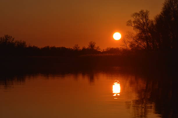Sunset on the river with willows in the foreground and reflection in the water in early spring