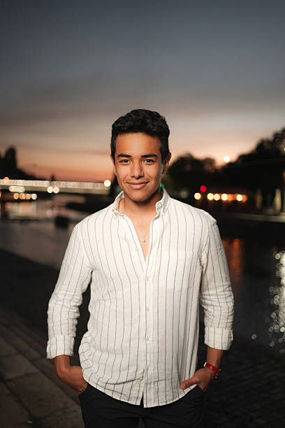 Portrait of a young latino man smiling with hands in pockets in Paris near the Seine river at sunset