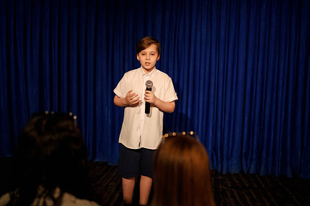 istock Boy speaking on stage with microphone in front of audience 2232906594