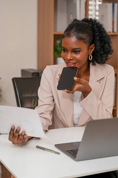 Professional woman engages creative collaboration using technology, connecting with others while reviewing documents and speaking her smartphone. This scene captures essence of modern work life
