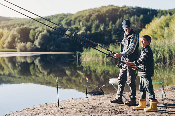 istock Father and son standing side by side holding fishing rods 2232915540