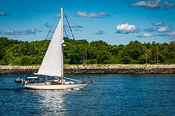 A small one masted yacht powers east on the Cape Cod canal on a late August morning.  Due to marine regulations, sailboats must use power when using the canal.