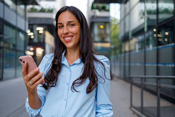 istock Smiling young businesswoman using her smartphone while standing in front of an office building, exuding confidence and positivity in an urban setting 2232918829