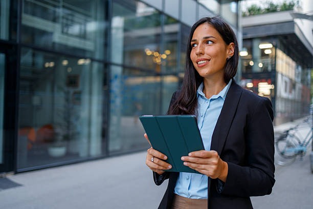 istock Professional woman navigating urban sidewalk, checking digital tablet with confident smile, modern skyscraper background 2232919081