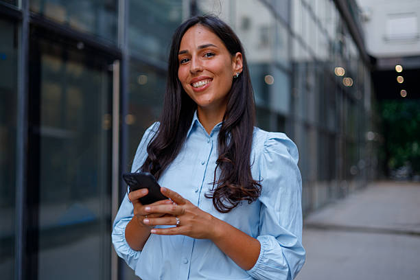 istock Professional woman smiling, working on smartphone near sleek downtown office structure during daytime 2232919224