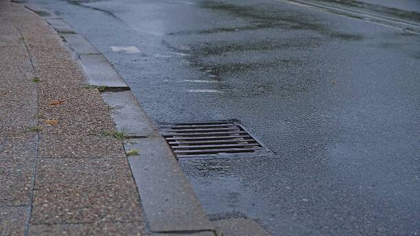 istock Rain Water Flowing into Storm Drain Grate by Street Curb 2232920301