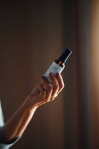 Hand Holding Glass Bottle with Spray Nozzle in Dramatic Lighting
