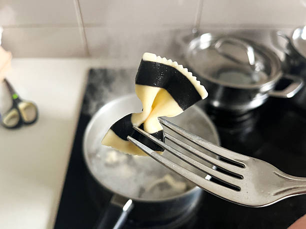 the preparation of a gourmet squid ink pasta dish in a cozy domestic kitchen. The striking contrast of the black and white bow tie pasta adds a touch of elegance to this classic Italian culinary experience