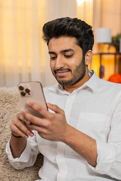 istock Indian man sits on sofa focused on smartphone typing text reading news responding to messages work 2232930407