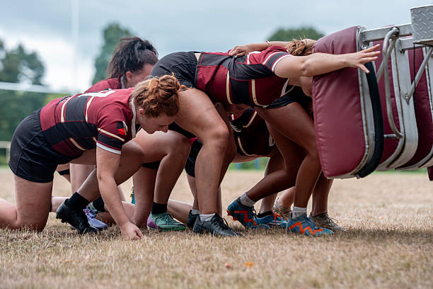 A diverse group of women rugby players actively engaging in training on a grassy field, showcasing teamwork and dedication. Their focus illustrates the strength and determination needed in sports.