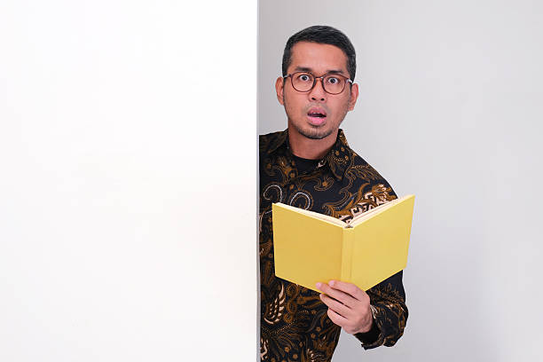 istock Indonesia teacher peeking behind wall holding a book with shocked face expression 2232934572
