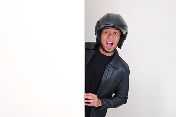 Motorcycle rider wearing helmet peeking behind wall with wow face expression