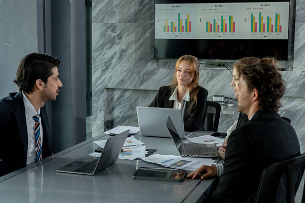 istock Business team gathering around boardroom table for strategy session with laptops financial reports pie charts and documents discussing company performance collaboration in workplace 2232946050