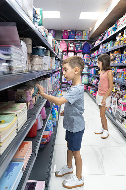 istock Elementary School Child standing in bookstore and looking for lunch-box. Back To School Shopping Concept. Shopping for school. Little boy trying to decide which lunch-box to buy. 2232951754