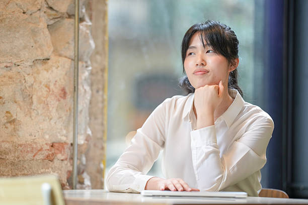 istock A woman sits at a table with her hands on her lap, looking out the window 2232953428