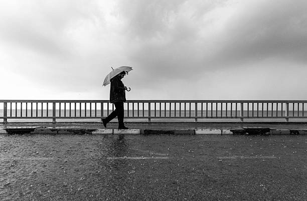 Man walking with an umbrella along the seafront during rainy weather, symbolizing solitude and melancholy.