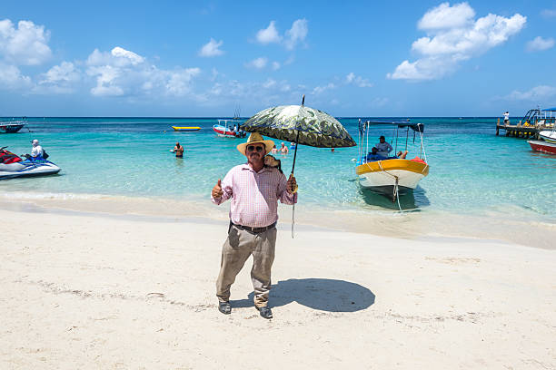 West Bay Beach, Roatan Island, Honduras - April 16, 2024: Man with monkey on shoulder poses on world-famous West Bay Beach in Roatan, Honduras.