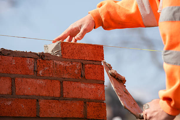 istock Close-up of skilled bricklayer working on construction site laying one more red brickin the wall 2232964318