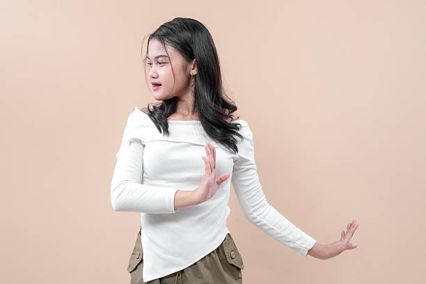 istock Asian woman in a white long sleeve top posing with expressive hand gestures, looking aside with confidence and natural elegance against plain background. 2232964513
