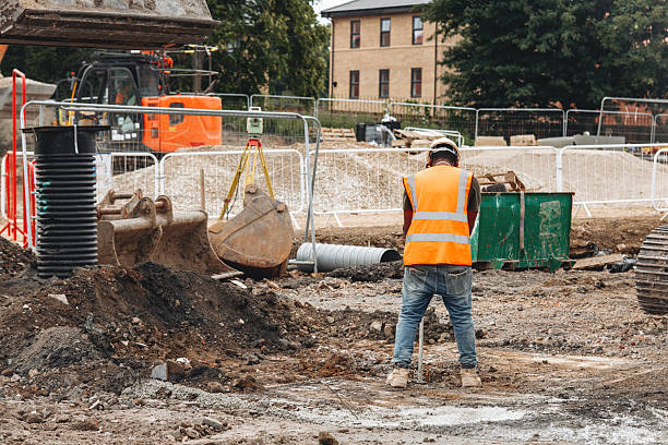 istock Builder surveyor focused on using surveying equipment while performing measurments at construction location, wearing bright safety hi-viz vest for visibility 2232964934