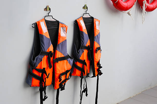 istock Two orange and gray life jackets hanging on wall hooks for safety use. 2232967578