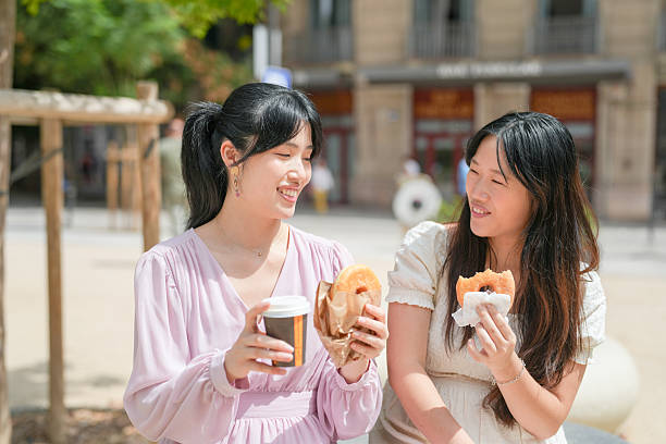 istock Two women are sitting on a bench and eating donuts 2232967875