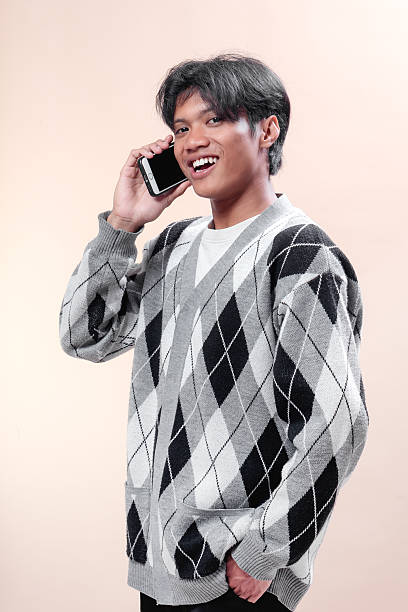 istock Asian man smiling while talking on smartphone, wearing stylish argyle sweater, showing confident and positive expression, modern communication concept. 2232968635