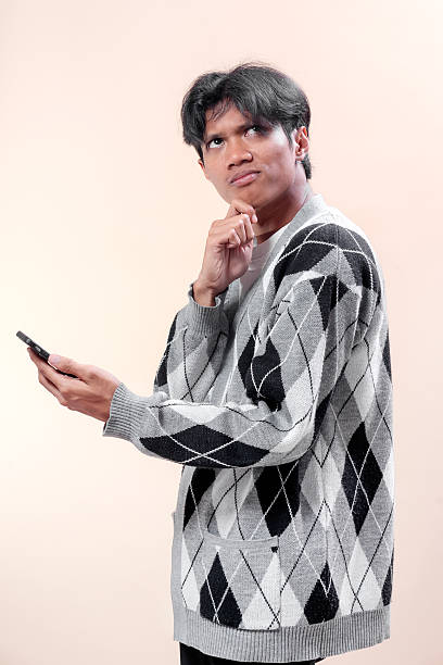istock Asian man holding smartphone with thoughtful expression, touching chin as if making a decision, symbolizing focus, business planning, modern lifestyle, communication, and professional concept. 2232969059