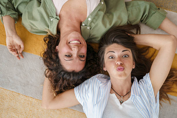 istock Two Young Female Friends Making Funny Faces While Lying On Carpet At Home 2232970370